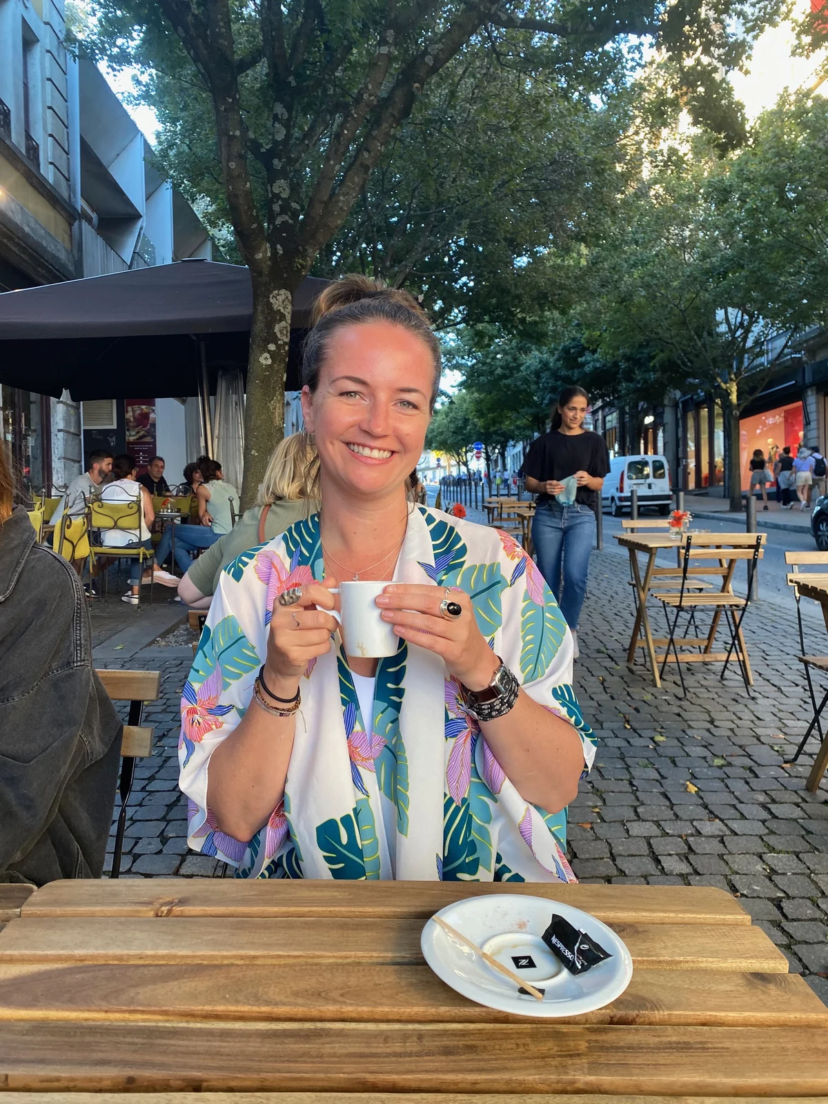 Pamela Sharkey, smiling, having coffee on a street terrace